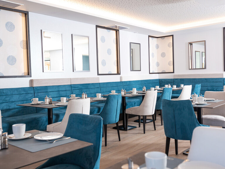 detailansicht-fruehstuecksraum-mit-spiegeln gemütliche-petrolfarbene-sitzbaenke-gedeckte-tische-spiegeln-und-beleuchtete-dekoelemente-an-der-wand