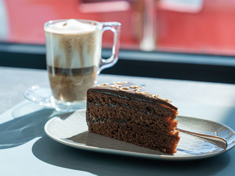 fruehstuecksraum-latte-macchiato-sachertorte sonnenlicht-faellt-auf-die-tische-gedeckt-mit-latte-macchiato-und-saftiger-sachertorte