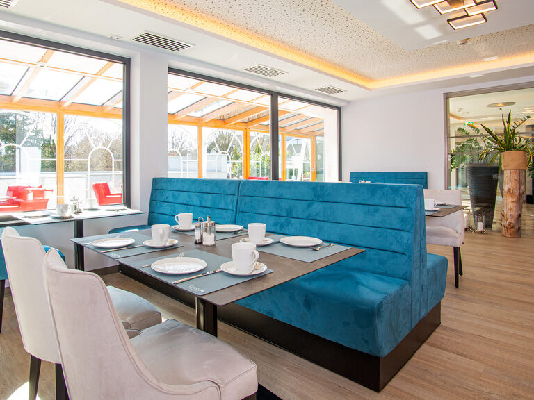 eingedeckter-fruehstuecksraum-mit-blick-zum-aussenpool aufnahme-vom-fruehstuecksraum-mit-blick-durch-die-fenster-und-den-hellen-wintergarten-zum-aussenpool-oder-zur-lobby-mit-dem-beruhigenden-brunnen