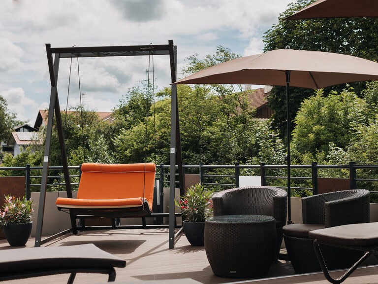schwebeliege-auf-sonnenterrasse einladende-schwebeliege-auf-unserer-sonnenterrasse-und-sitzgelegenheit-für-den-cocktail-am-nachmittag-umrankt-von-bluehenden-blumen