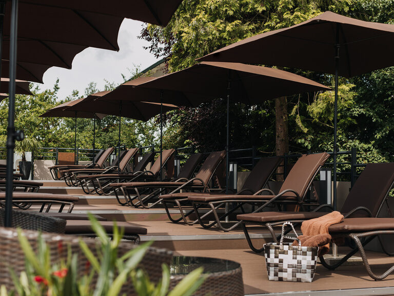 sonnenterrasse-mit-bequemen-liegenauflagen einladende-sonnenterrasse-mit-braunen-moebeln-bequemen-auflagen-erholsamen-relaxliegen-schattenspendenen-sonnenschirmen